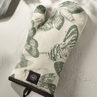 Lifestyle image of Kew Living Jewels Single Oven Glove with light grey background and illustrations of insects including moths and butterflies.