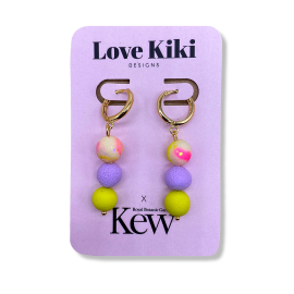 Love Kiki x Kew earrings featuring three pom pom clay balls in green, purple and pink/white. Gold hoop clasp and placed on card packaging which reads Love Kiki designs, Royal Botanic Gardens Kew.