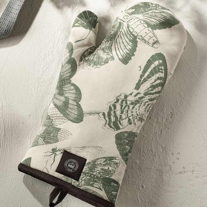 Lifestyle image of Kew Living Jewels Single Oven Glove with light grey background and illustrations of insects including moths and butterflies.