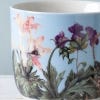 Close up of blue Kew mug featuring a floral design with a bee pollinating a pink flower.