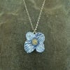 Image of the necklace featuring a poppy-shaped pendant enameled in pale blue colour. The necklace chain is in metal silver and it lays on a marbled surface