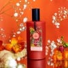 Red bottle of the Bergamot and Ginger Eau de Toilette with label and black lid. Red background with bergamot and ginger surrounding.