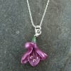 Image of the necklace featuring a freesia flower-shaped pendant in pink-purple colour. The necklace chain is in metal silver as the casting of the pendant and it lays on a marbled surface