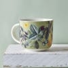 Light green Kew mug featuring a floral and fruit design with a small yellow butterfly on a white wooden surface with a grey backdrop.