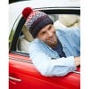 Lifestyle image of the Clifden Beanie Hat with a red bobble on top and a grey, red and blue pattern.