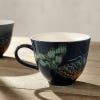 Lifestyle image of Kew midnight blue china mug with blue handle features detailed artwork of insects from Kew's archives.