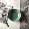 Cereal bowl on white table with tea towels from the range and a spoon surrounding. 