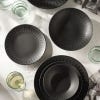 Lifestyle image of six plates and bowls from the range on table with glasses and tea towels to complement.