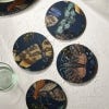 Lifestyle image of midnight blue four cork-backed coasters featuring the intricate artwork from the famous Royal Botanic Gardens, Kew's archives. Intricate patterns and colours from a diverse range of bugs.